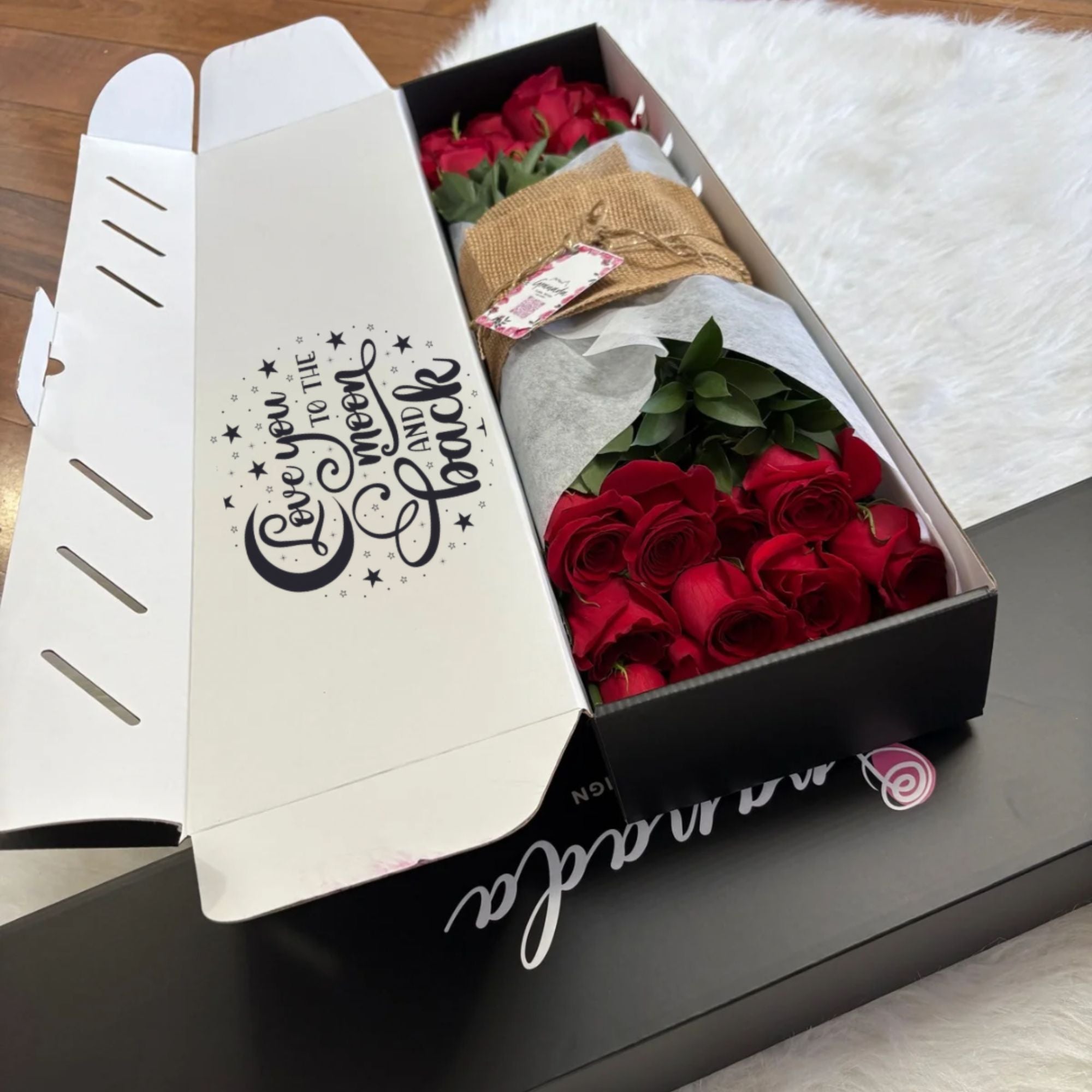 Box with red roses and a small brown bag on a white surface