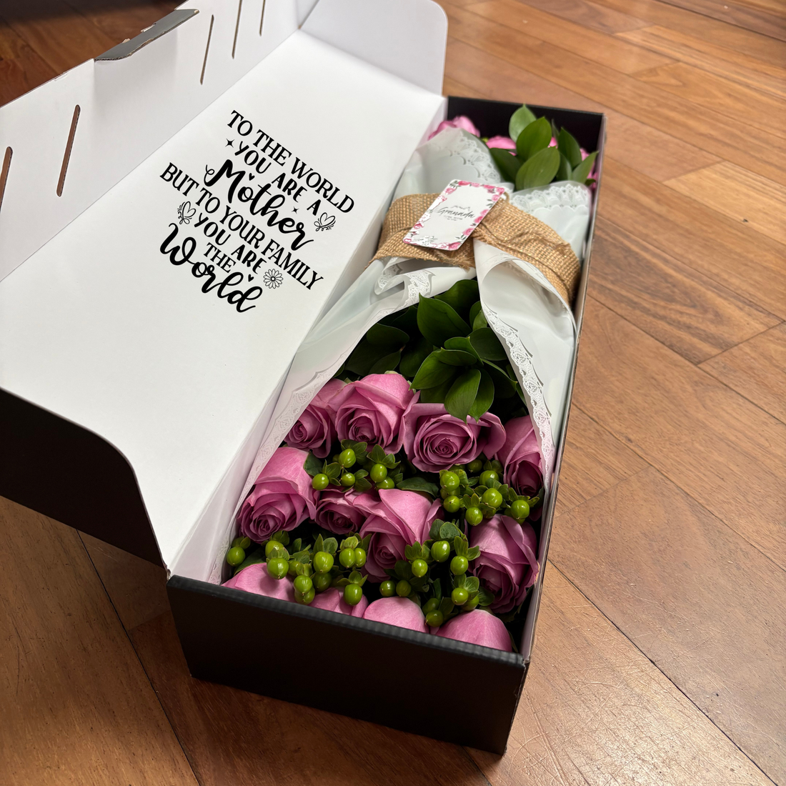 Bouquet of red roses in a black box with 'love' text, surrounded by flowers on a light background.