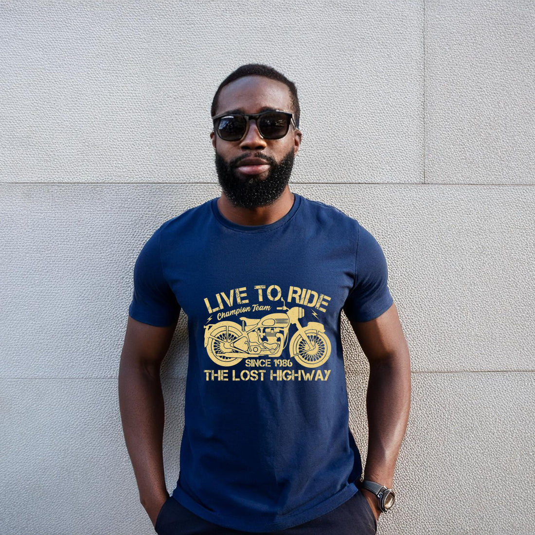 Man wearing an olive green “Live to Ride” motorcycle t-shirt with a vintage motorbike print, standing in an urban setting.