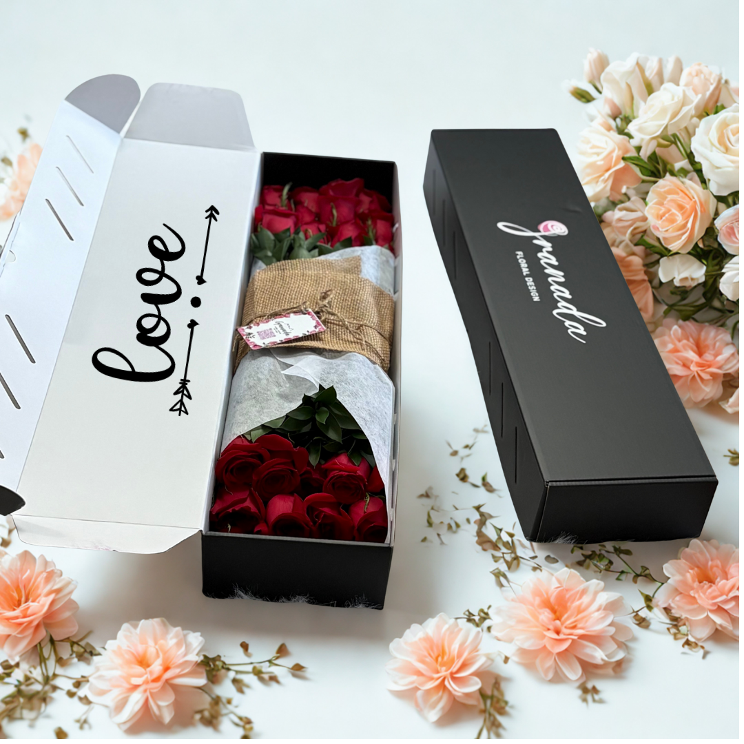 Bouquet of red roses in a black box with 'love' text, surrounded by flowers on a light background.
