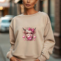 sand  sweatshirt with a highland cow graphic wearing a pink bow and blowing bubblegum, surrounded by pink hearts.