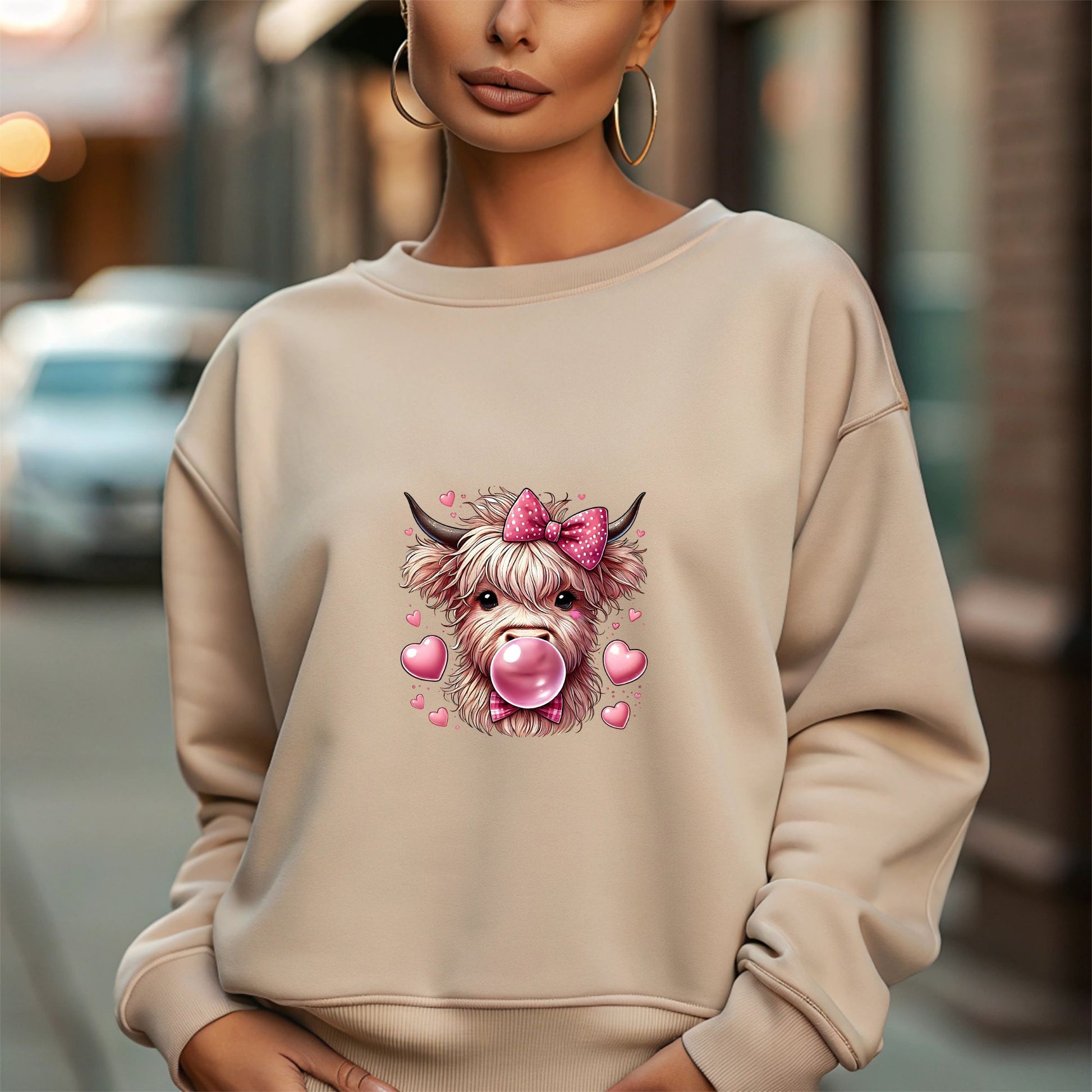 sand  sweatshirt with a highland cow graphic wearing a pink bow and blowing bubblegum, surrounded by pink hearts.