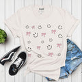 Cute Smiley & Bow Graphic T-Shirt in white, paired with ripped denim shorts and sandals. Trendy aesthetic outfit.